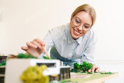 Preview: Photo of joyful young woman architect designing draft with house model