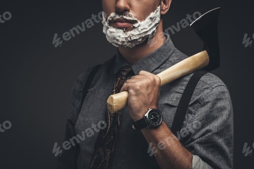 Preview: Cropped shot of man with shaving cream on his face, holding an axe