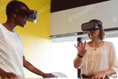 Preview: Diverse businesswomen standing at desk using vr headset at work