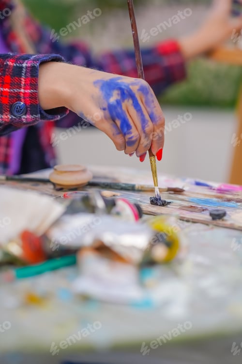 Preview: Close-up of a girl painter's hands in paint who takes oil paint from a palette with a brush painting
