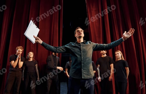 Preview: Man is practicing his role. Group of actors in dark colored clothes on rehearsal in the theater