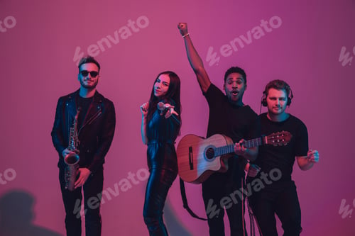 Preview: Group of young multiethnic musicians created band, dancing in neon light on pink background