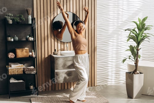 Preview: Happy woman listening music with headphones and dancing in modern bathroom