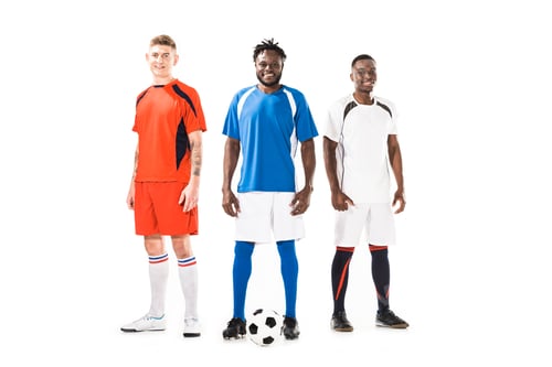 Preview: happy young athletic multiethnic soccer players standing together and smiling at camera isolated on