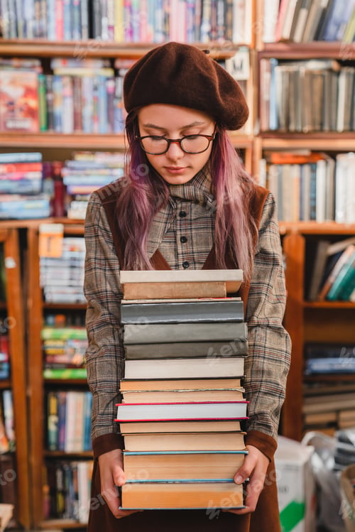 Preview: Young clever good-looking caucasian female student holding a stack of books in library or bookstore.