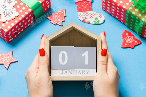 Preview: Top view of female hands holding calendar on blue background. The first of January