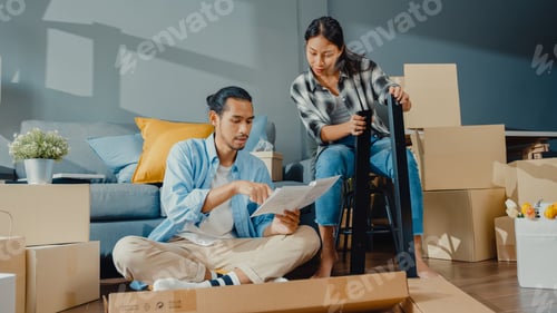 Preview: young attractive couple man and woman help each other unpacking box and assemble furniture.