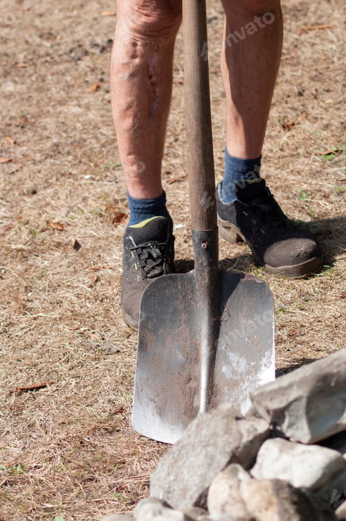 Preview: gardener in dirty work clothes and boots holds garden tool shovel,seasonal spring work in the garden