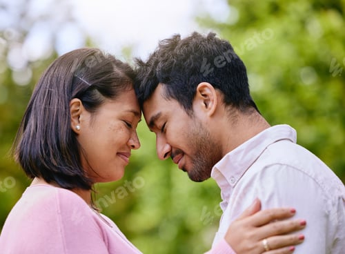 Preview: Smiling Asian couple standing together with their foreheads touching each other against nature back