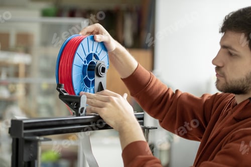 Preview: Young designer putting spool with red filament in 3d printer to print new items