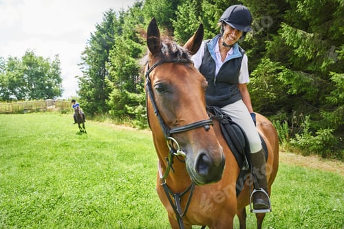 Preview: Mature woman on horseback wearing riding hat and boots looking at horse smiling