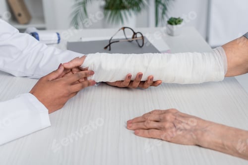 Preview: Cropped view of african american doctor touching and checking broken arm of patient