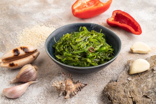 Preview: Chuka seaweed salad in blue ceramic bowl on brown concrete. Side view