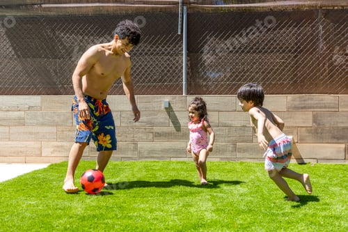 Preview: Father plays soccer with his children in the backyard on a sunny day, having fun.