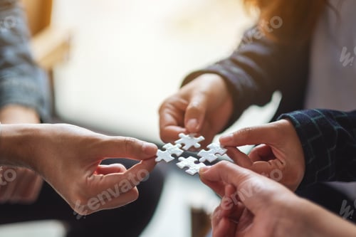 Preview: Closeup image of a group of people holding and putting a piece of white jigsaw puzzle together