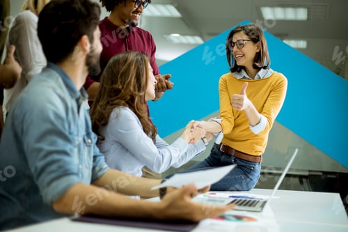 Preview: Group of young coworkers interacting around a table and handshaking in the office