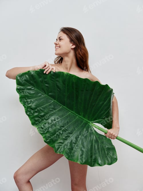 Preview: cheerful woman with a naked body a large green leaf in her hands light background