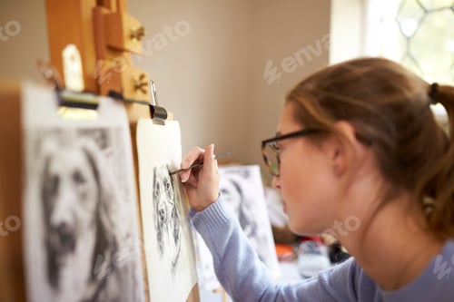 Preview: Side View Of Female Teenage Artist Sitting At Easel Drawing Picture Of Dog From Photograph
