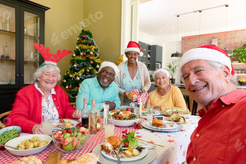 Preview: Diverse group of happy senior friends in holiday hats celebrating christmas together, taking selfie