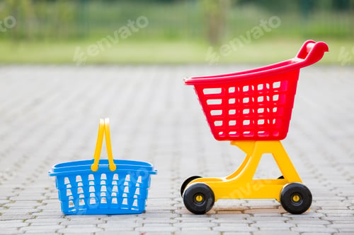 Preview: Bright plastic colorful toys, shopping cart and basket outdoors on sunny summer day.