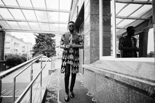 Preview: African stylish and handsome man in traditional outfit and sunglasses standing outdoor.