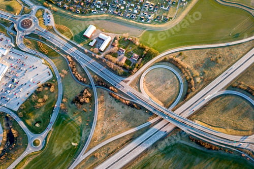 Preview: Aerial top view of modern highway road intersection, house roofs on spring green field