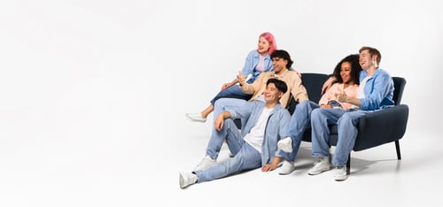 Preview: Happy teen multiracial friends watching movie, sitting on sofa and floor, looking at free space