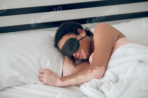 Preview: Young woman in a mask for sleep lying in bed
