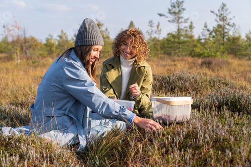 Preview: Two young cheerful girls spending weekend in countryside picking autumn berries and communicating