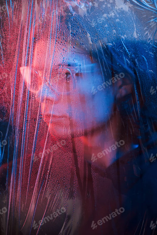 Preview: Side view. Studio shot in dark studio with neon light. Portrait of serious man behind the wet glass