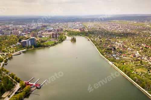Preview: Aerial view of city lake among green trees and town buildings in recreation park zone. Drone