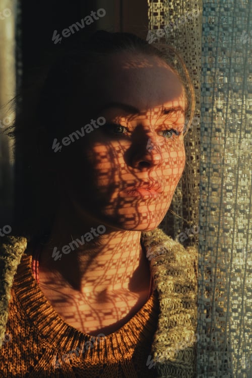 Preview: portrait of a woman standing next to a window, sunset through curtain cast a shadow on her face