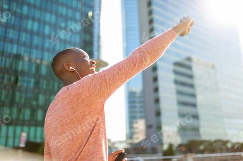 Preview: Side of young black man punching the air, listening to music with earphones and cellphone