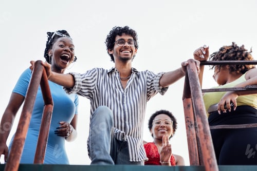 Preview: Four cheerful multiethnic friends descend the iron ladder from the roof of the house