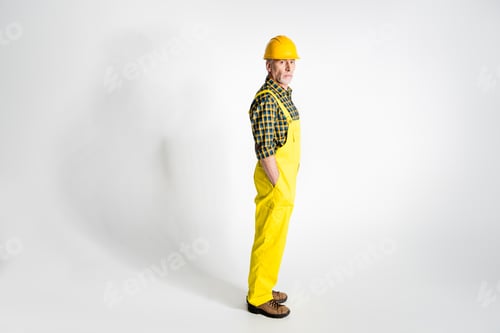 Preview: Full length portrait of mature workman in hard hat looking at camera isolated on grey