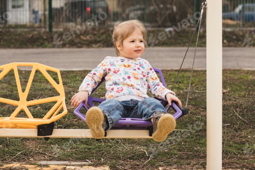 Preview: A little cheerful girl having fun, riding on a colorful swing in a city park
