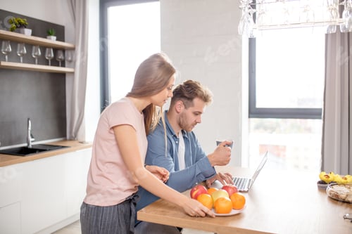 Preview: young couple watching video from the laptom in the kitchen with modern interior