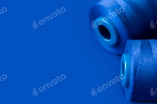 Preview: texture of blue thread in spool for sewing on a plain blue background. close up. clothing sewing mat