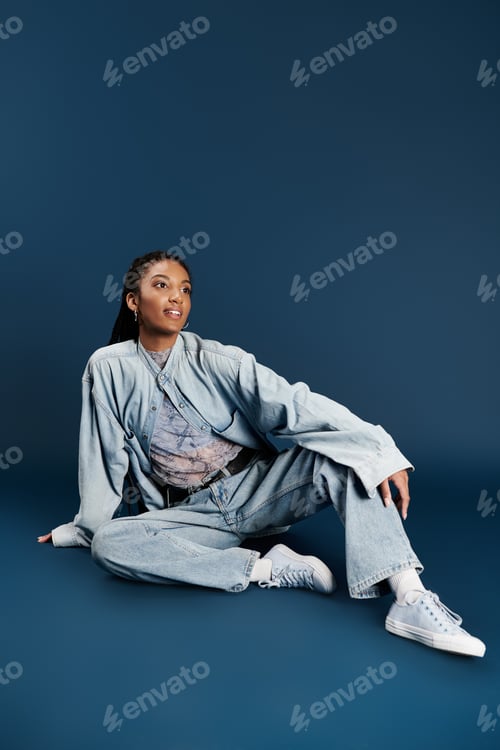 Preview: A stylish young woman poses gracefully in denim against a deep blue backdrop