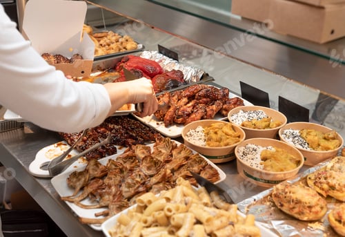 Preview: the hand of an unrecognizable person putting chicken wings into a paper box at a food counter