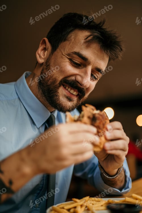 Preview: Happy businessman eating burger and french fries in restaurant