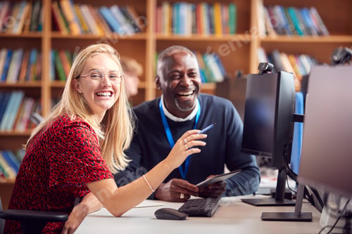 Preview: Female University Or College Student Working At Computer In Library Being Helped By Tutor