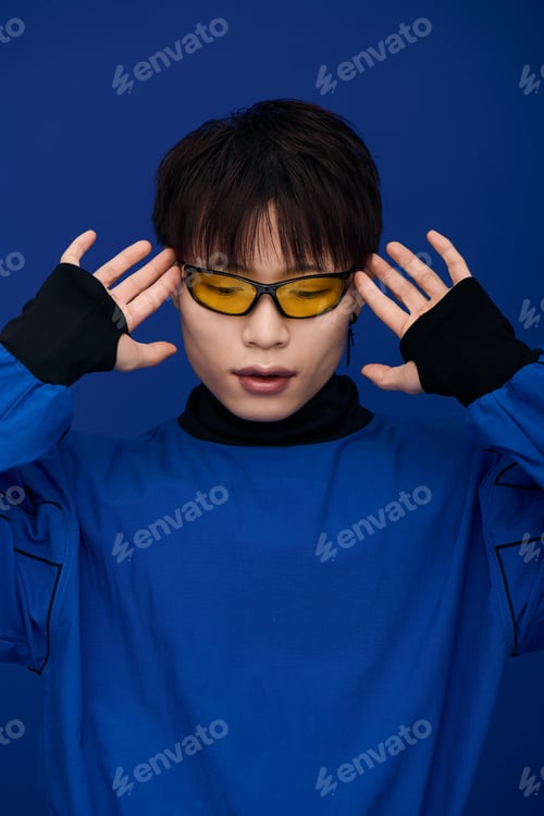 Preview: Striking young asian man poses with stylish sunglasses against a vivid blue backdrop