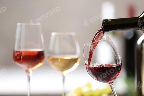 Preview: Pouring red wine from bottle into glass on blurred background. Space for text