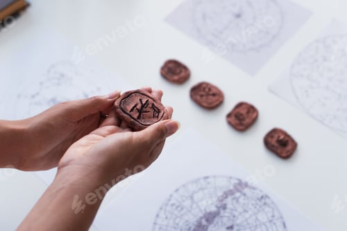 Preview: high angle view of cropped fortune teller holding clay rune near blurred star charts