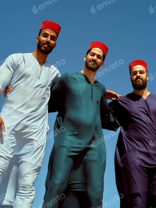Preview: Three men in traditional attire and red fez hats posing against a clear blue sky, Morocco