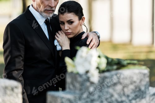 Preview: selective focus of bearded man in suit hugging attractive woman in graveyard