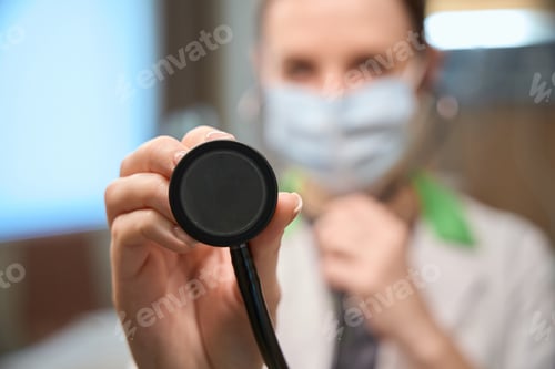 Preview: Health worker in protective mask holds stethoscope in his hands
