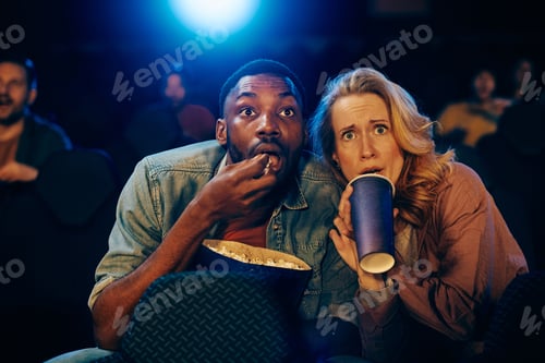 Preview: Multiracial couple watching suspense thriller in movie theater.