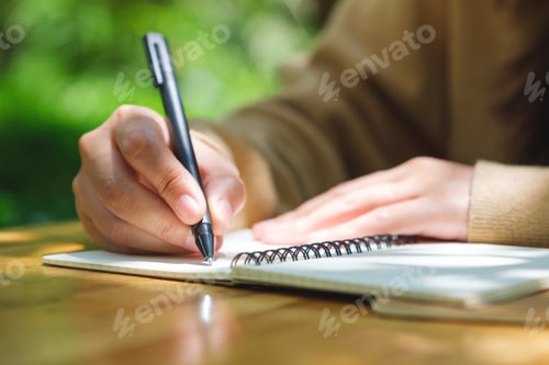 Preview: Closeup image of a woman writing on a notebook in the outdoors